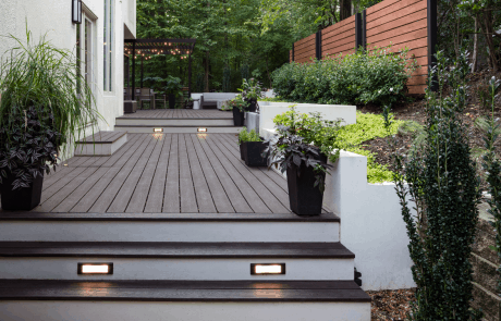 luxurious multi-level deck features a modern and functional design with an expansive Trex deck separated by modern white concrete retaining walls with Fire Feature