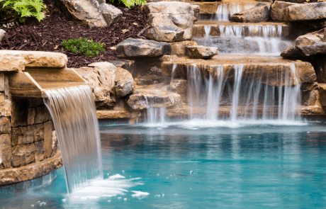 Free form custom swimming pool and stacked stone raised spa features boulder walls, and a gorgeous field stone waterfall that includes a stone bench under the waterfall.