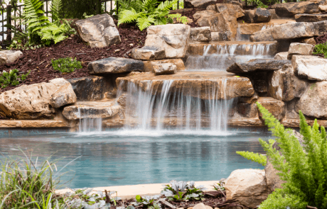 Free form custom swimming pool features boulder walls and native landscaping, including a stream and water feature that winds its way through the boulder garden.