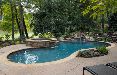 Backyard remodel in Johns Creek includes a free form custom swimming pool and stacked stone raised spa with a waterfall spillover, underwater stone bench, flagstone coping and boulder waterfall. The patio is decorative stamped concrete and overlooks the golf course.