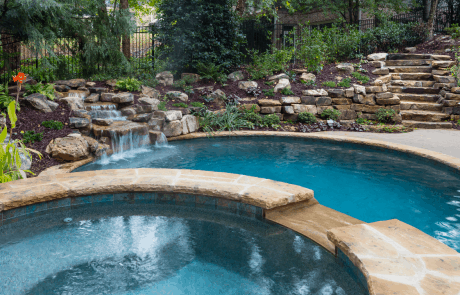 Free form pool with a stacked stone raised spa and waterfall spillover, a boulder waterfall, flagstone coping and Verona 'Boticas pool tile. The Crab Orchard TN Flagstone Stepper pathway and native landscaping blends perfectly with the natural surroundings.