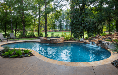 Free form custom swimming pool features a circular stacked stone raised spa with a waterfall spillover, underwater stone bench, flagstone coping and boulder waterfall. The patio is decorative stamped concrete and overlooks the golf course.