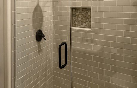Nature inspired pool house bathroom includes a walk-in shower with glass doors and a black matte hinged shower door, a white honed pebble mosaic tile floor with coordinating niche, and gray ceramic subway tile shower walls.