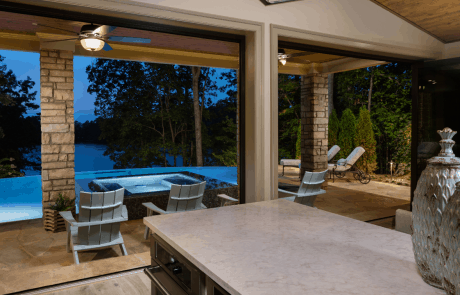 Custom pool house design includes an open concept floor plan with vaulted ceilings and black accordion doors that open to the outdoors providing a seamless indoor-outdoor connection and breathtaking views of the infinity edge pool overlooking Lake Lanier.