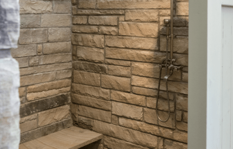 Outdoor shower features a stacked stone knee wall and stone bench with a flagstone floor and cedar tongue and groove wall.