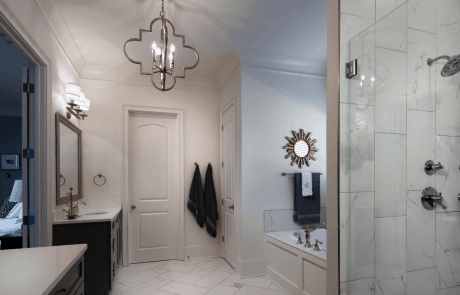 Transitional master bathroom with separate vanities, under mount sinks, white quartz countertops, brown shaker cabinets, polished nickel fixtures, white soaking tub, glass enclosed shower, and a four light pendant chandelier.