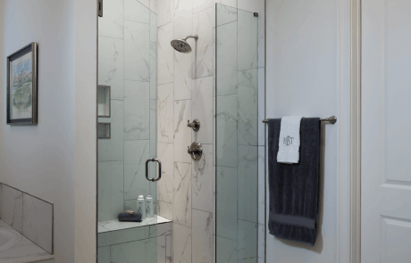 Master bathroom with a glass enclosed shower, seating bench, polished chrome fixtures and white porcelain wall tile.