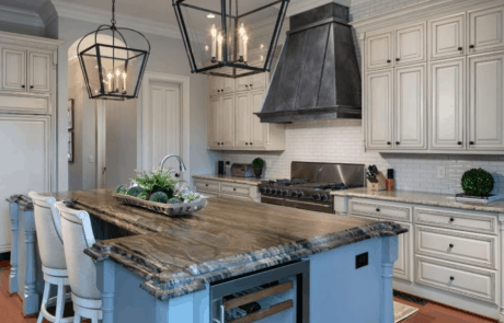 Kitchen features White Raised Panel Cabinets, a Large Kitchen Island with Granite Countertops, Over-Sized Bronze Pendant Lights, White Beveled Tile Backsplash