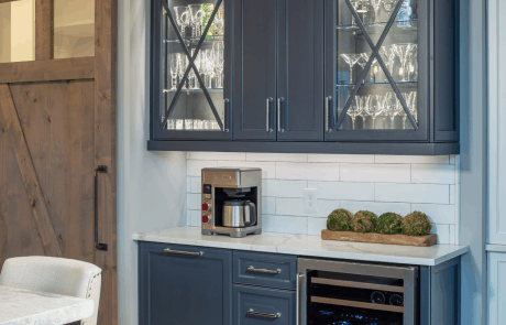 Kitchen remodel includes a custom coffee/beverage station in blue with built-in wine fridge and storage, Quartzite countertops, white shaker cabinets with glass cabinet doors and white subway tile backsplash.
