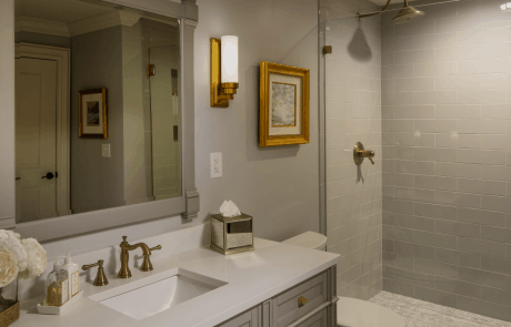 Transitional bath remodel features a single sink gray vanity with a white quartz counter-top and undermount sink with satin brass plumbing fixtures and vanity sconces.