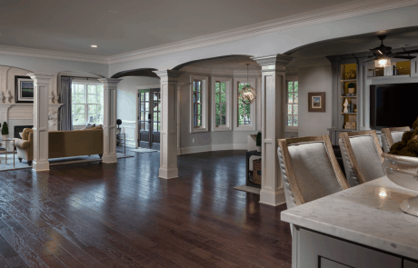 The large central living space acts as the hub for this custom basement remodel and includes dark brown hardwood floors, a custom designed kitchen and bar island