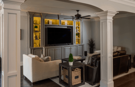 Custom basement remodel with separate TV area features a gray custom built-in entertainment center complete with inset lighting and storage, dark brown hardwood floors and comfortable seating.