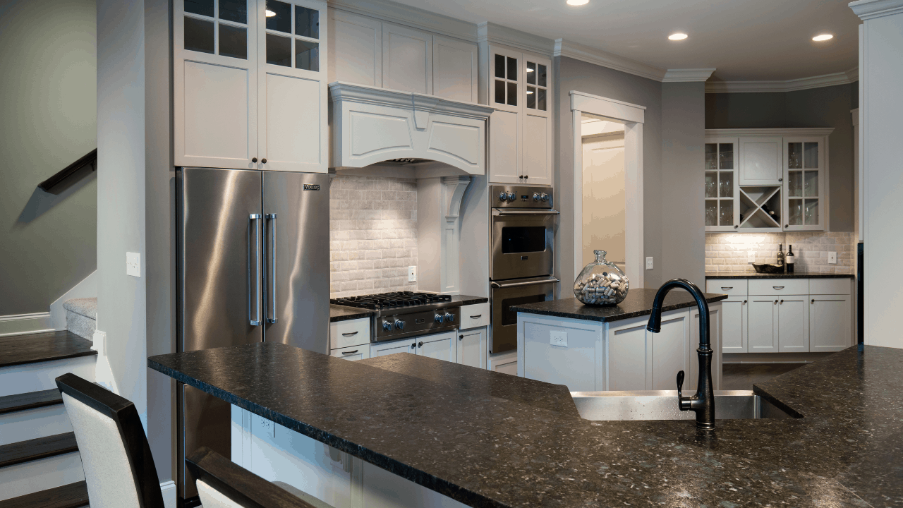 The spacious modern transitional kitchen features an eat-in-kitchen, breakfast bar, island, and separate coffee station with black leathered granite countertops, floor to ceiling white shaker cabinets with black hardware and stainless-steel appliances.