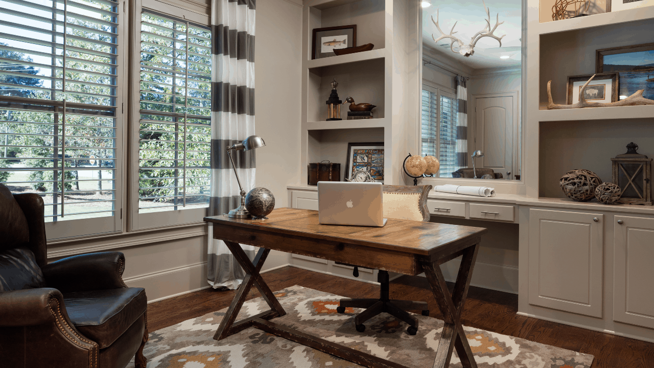 The private home office, painted in Benjamin Moore’s Revere Pewter, features custom built-in book shelves, crown molding and large windows for plenty of natural light. The large classic, freestanding desk, brown leather arm chair and geometric gold and orange rug creates a warm and timeless look.