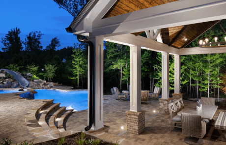 Tennessee flagstone and field stone boulders create a raised wall for the fun custom water slide in this freeform pool. Wide flagstone steps lead to a custom poolside cabana featuring a stacked stone fireplace and outdoor pizza oven combo, covered outdoor dining room, private bathroom, stained tongue & groove ceiling with white painted posts and cornice, Hardie Shake siding, and gable roof.