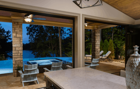 Custom pool house design includes an open concept floor plan with vaulted ceilings and black accordion doors that open to the outdoors providing a seamless indoor-outdoor connection and breathtaking views of the infinity edge pool overlooking Lake Lanier.
