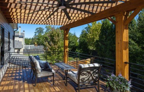 upper cedar deck is covered with a modern style pergola and includes a custom black wrought iron railing, large outdoor ceiling fans, comfortable lounge seating