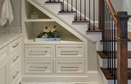 Under stair built-in custom cabinets with open shelving and chrome fixtures. New staircase with brown hardwood steps and black metal balusters.