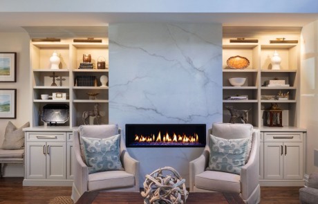 Keeping room renovation includes a seating area with a white porcelain slab surround and modern linear fire feature, custom built-in cabinetry and trim work, and brown hardwood floors.