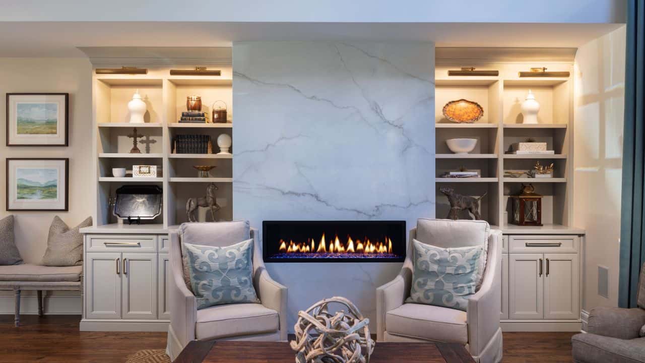 Keeping room renovation includes a seating area with a white porcelain slab surround and modern linear fire feature, custom built-in cabinetry and trim work, and brown hardwood floors.