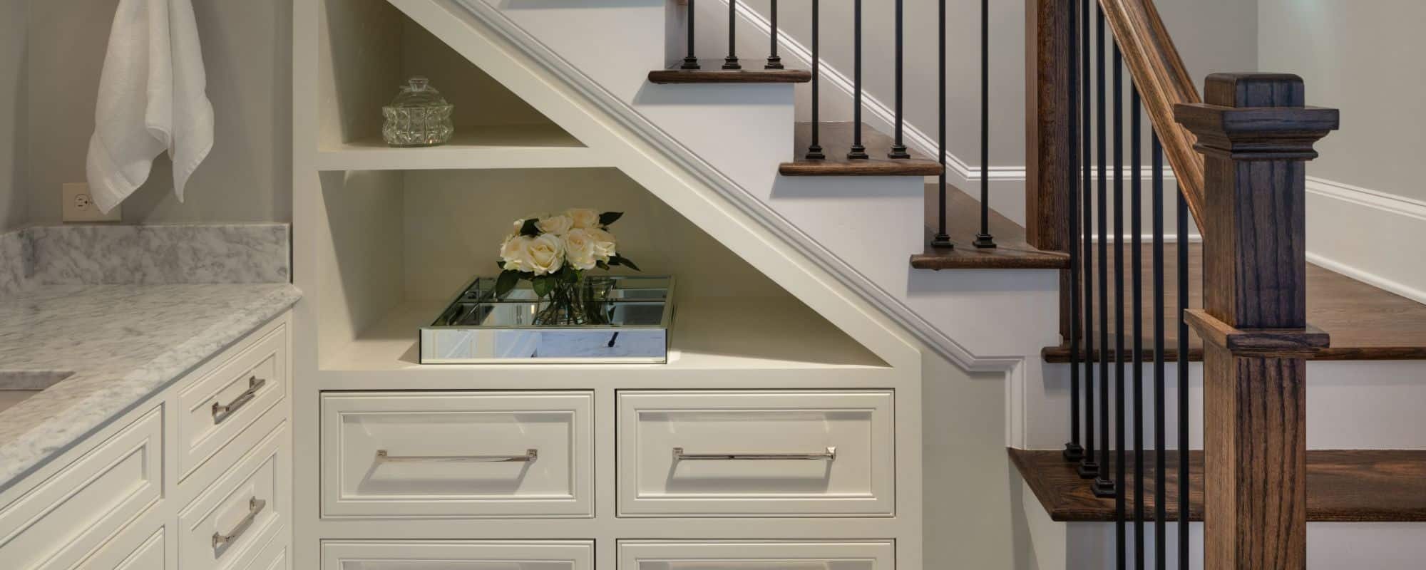 Under stair built-in custom cabinets with open shelving and chrome fixtures. New staircase with brown hardwood steps and black metal balusters.