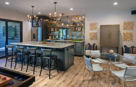 Modern Basement Remodel with Kitchen, Bar Island w/Seating, Charcoal Cabinets, Caesarstone Quartz Countertops, Stainless Steel Appliances, Mirrored Backsplash, Floating Shelves, Brass Pendant Lights, Panoramic Doors and Glass Game Table.