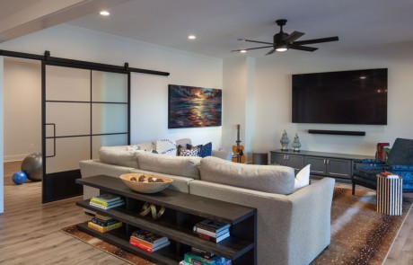 Basement Remodel includes a Sophisticated Living Space with 85” TV and Comfortable Seating. Oversized Metal & Glass Sliding Doors lead to the Custom Home Gym.