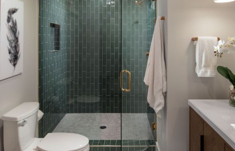 Basement Remodel includes a full bathroom with a sage colored, glass-tile, walk-in shower, and brushed gold accents. Hexagon, porcelain, tile flooring, brown, freestanding vanity, white marble countertops, undermount sink, and drop style pendants.