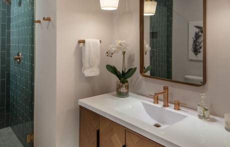 Midcentury style freestanding vanity with white marble countertops, undermount sink, gold hardware, rectangular gold mirror, and drop style pendants.