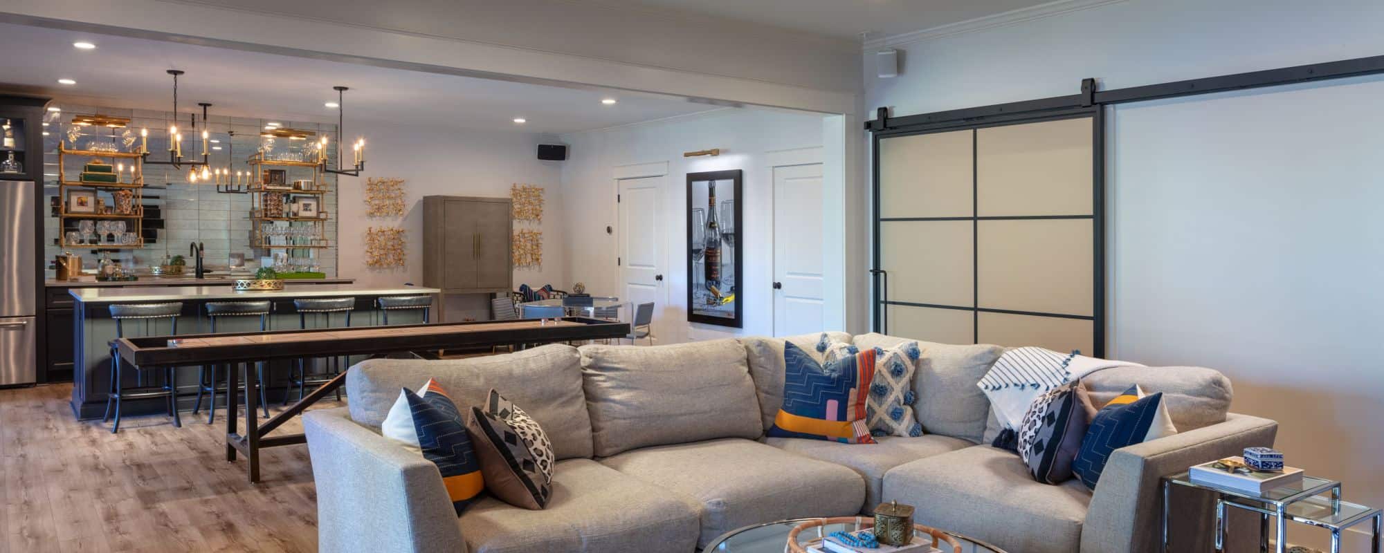 Basement Remodel with Kitchen, Bar Island w/Seating, Charcoal Cabinets, Caesarstone Quartz Countertops, Stainless Steel Appliances, Mirrored Backsplash, Floating Shelves, Brass Pendant Lights, Custom Shuffleboard Table and Metal & Glass Barn Doors.