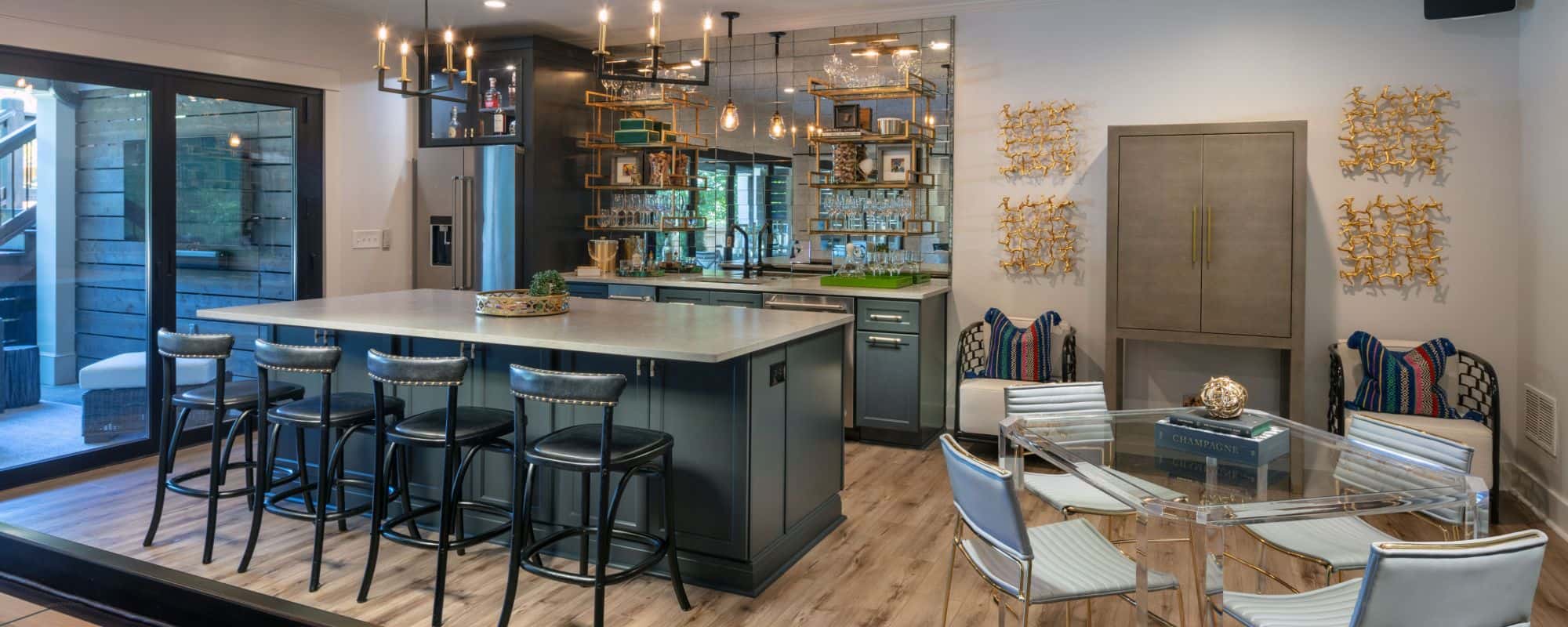 Modern Basement Remodel with Kitchen, Bar Island w/Seating, Charcoal Cabinets, Caesarstone Quartz Countertops, Stainless Steel Appliances, Mirrored Backsplash, Floating Shelves, Brass Pendant Lights, Panoramic Doors and Glass Game Table.