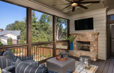 The screened in porch includes a stone fireplace with mounted tv, white shiplap walls, tongue and groove ceiling, brown ceiling fan and comfortable seating.