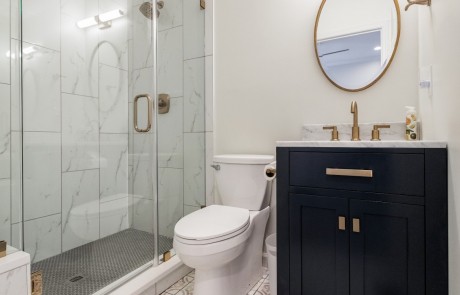 Modern blue and gold guest bathroom features a 24” navy blue vanity with white marble countertop