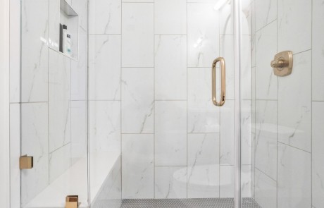 Modern frameless glass shower enclosure with hinged door features a champagne bronze shower faucet