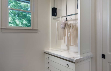 Custom Laundry Room with gray porcelain tile floor, white custom cabinets, solid surface countertops and custom hanging drying station and drying rack drawers.