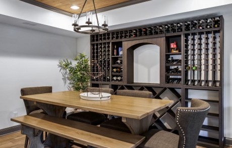 Custom basement renovation includes a private wine cellar and wine tasting room with floor-to- ceiling wine racks and shelves that can house 425 bottles of wine. A round metal chandelier above the large farmhouse table complements the Stikwood ceiling and provides the perfect setting for wine tasting with guests.