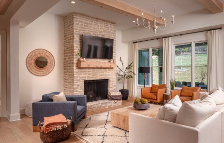 This large transitional living room with its exposed beams and wall of windows is timeless and inviting and embraces the same warm, natural textures and clean lines used throughout the home. A comfortable white couch and a pair of terracotta leather chairs surround a stunning limestone fireplace with mounted tv and floating mantle.