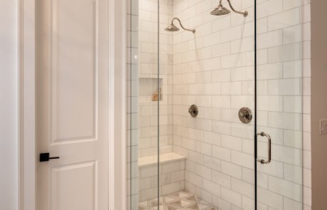The frameless glass shower enclosure with hinged door boasts dual rain shower heads with separate controls, built-in bench and shampoo niche and a marble tile mosaic shower floor.