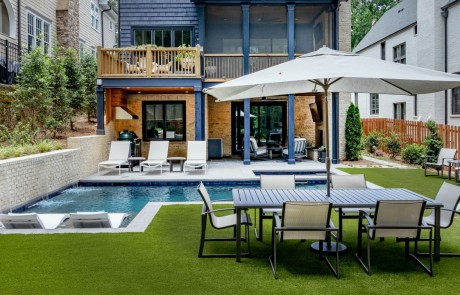 Contemporary backyard oasis in the heart of Atlanta is the ultimate indoor-outdoor living space featuring a modern plunge pool and spa with a sheer decent pool wall and tanning shelf with loungers. Covered porch with bluestone paver patio, covered outdoor kitchen with custom vent hood, modern aluminum outdoor cabinets, concrete countertops, outdoor living room with brick fireplace and artificial turf lawn.