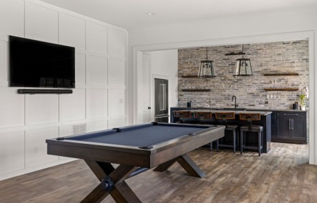Sophisticated black bar and billiard room with decorative trim paneling walls and mounted tv, black shaker cabinets, grey reclaimed brick backsplash, black pearl leathered granite countertops.