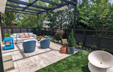 Modern backyard design with paver patio, covered steel pergola, artificial turf & lush landscape.