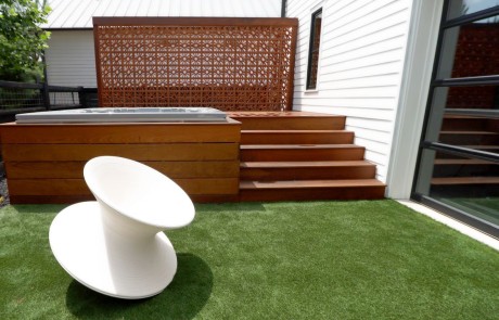 Small outdoor living space with modern style Ipe wood hot tub and raised deck, Breeze Block privacy screen walls, and artificial turf.