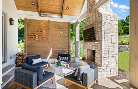 Modern indoor-outdoor living space with covered porch addition features a lounge area with wood burning limestone fireplace & mounted tv, paver patio, vaulted tongue & groove ceiling with ceiling mounted infrared heaters, and privacy screen walls.