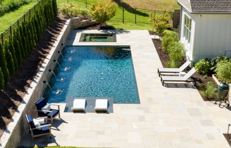 Custom backyard renovation features a contemporary swimming pool with flush spa, tanning ledge with in-pool loungers, and premium pool finishes surrounded by a Sandstone paver patio and lush landscaping.
