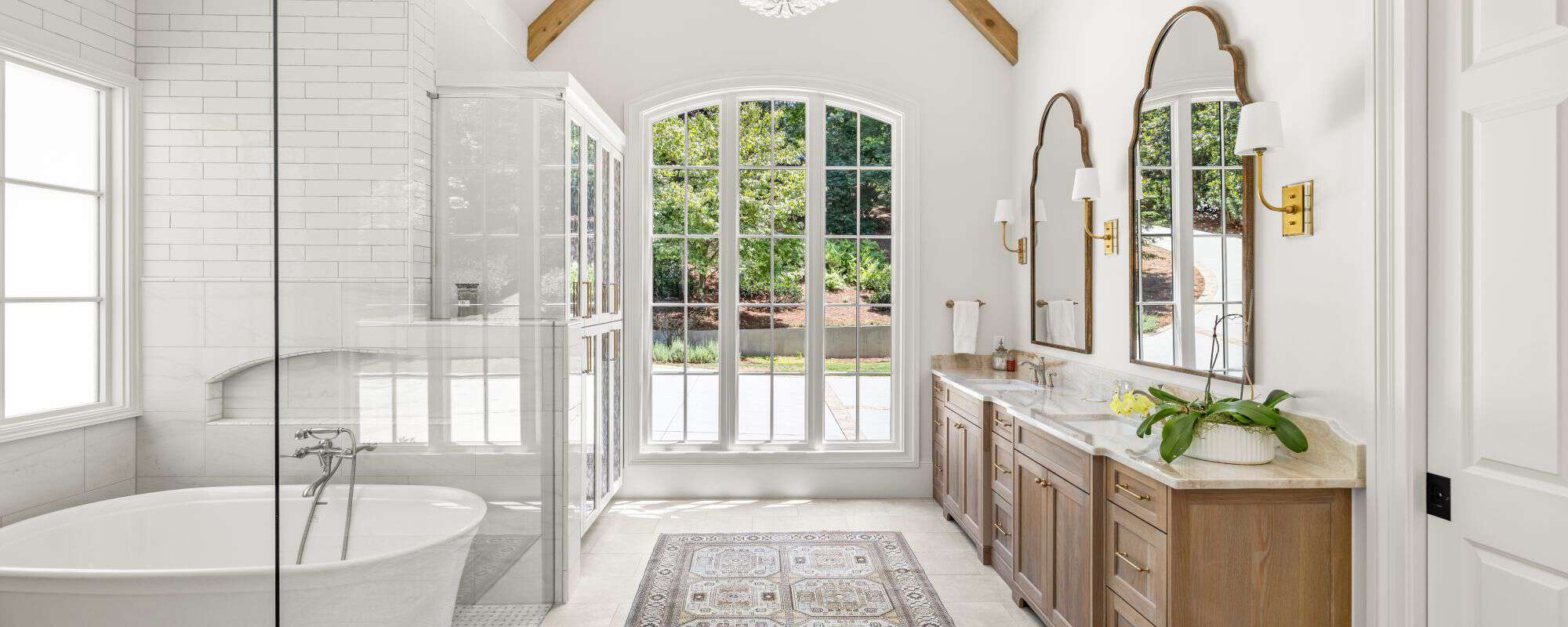 Luxury master bathroom renovation includes vaulted ceiling with a white and natural wood bathroom aesthetic, spa-like wet room with floor to ceiling white subway tile walls, freestanding soaking tub and high-end bathroom features.